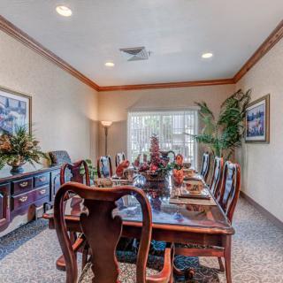 A well-decorated dining room with a long table set for a meal, surrounded by elegant chairs and adorned with artwork and plants.