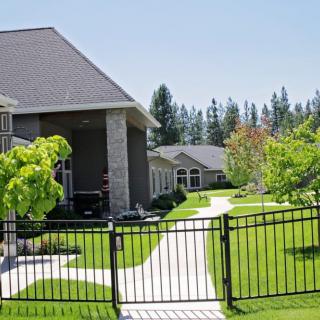 A suburban house with a well-maintained lawn and pathway, enclosed by a metal fence.