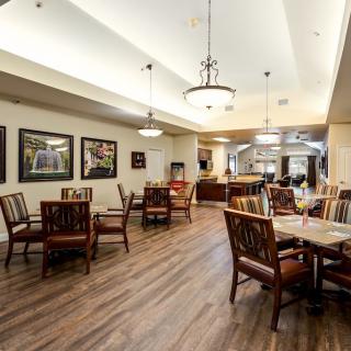 An elegant dining area with wooden flooring, furnished with tables and chairs, and adorned with wall art and ceiling lights.