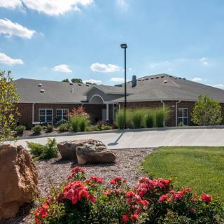 A residential house with a landscaped garden featuring flowers and a driveway under a clear blue sky.