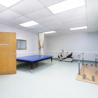 A clean and well-equipped therapy room with a blue exercise mat and physical therapy apparatus.