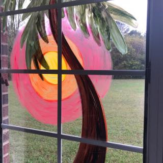 A beautifully colored glass decoration of a palm tree and sunset seen through a window.