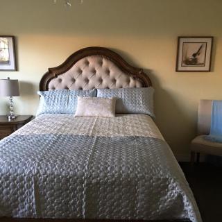 A cozy bedroom with a large bed featuring a tufted headboard, flanked by two side tables and decorated with framed wall art.