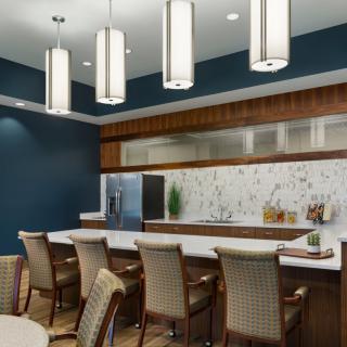 A modern kitchen interior with bar seating, contemporary lighting fixtures, and a marble backsplash.