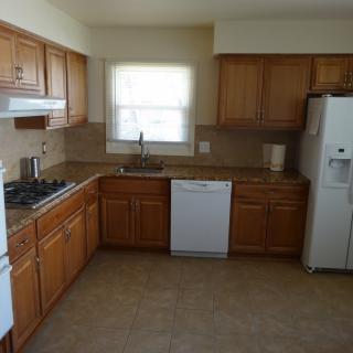 A kitchen with wooden cabinets, featuring a stove, dishwasher, and refrigerator.