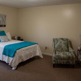 A cozy bedroom with a single bed, adorned with teal and white linens, accompanied by a patterned armchair.