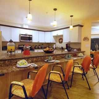 A modern kitchen and dining area featuring a long countertop with orange bar stools and pendant lighting.