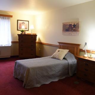 A cozy bedroom with a single bed, dresser, and soft lighting.