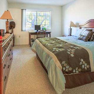 A cozy bedroom with a neatly made bed, a dresser, and a window letting in natural light.