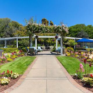 A beautifully landscaped garden featuring a pathway leading to an archway adorned with greenery and flowers.