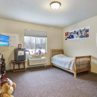 A cozy bedroom with a single bed, TV, and toys near the window.