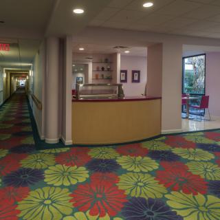 A hotel hallway with a colorful patterned carpet and a lobby area.
