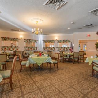 A spacious dining room with multiple tables covered in green tablecloths, elegant chairs, and a chandelier overhead.