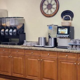 A hotel breakfast area featuring a coffee machine, juice dispensers, and wooden cabinets.