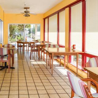 An empty restaurant interior with bright yellow walls and red window frames, featuring several wooden tables and chairs.