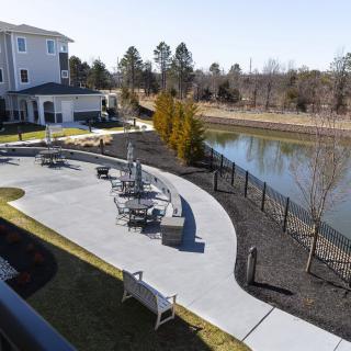 A serene outdoor patio area with tables and chairs overlooking a pond in a residential setting.