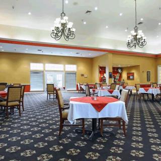 A spacious dining area with neatly arranged tables, elegant chandeliers, and bright lighting.