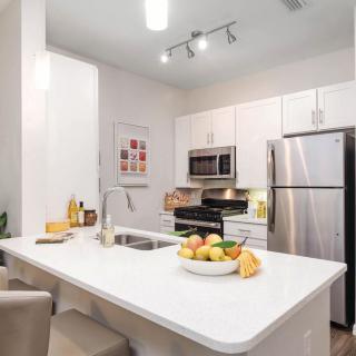 A modern kitchen with white cabinetry, stainless steel appliances, and a central island featuring a fruit bowl and bar stools.
