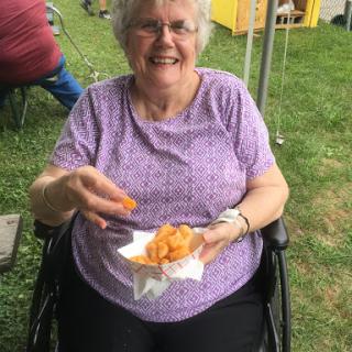 An elderly woman enjoying a snack while seated in her wheelchair at an outdoor event.