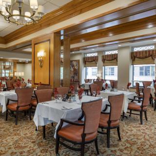 An elegant dining room with neatly arranged tables and chairs, featuring chandeliers and a carpeted floor.