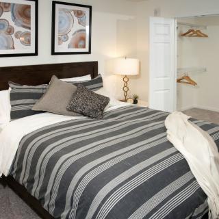 A modern bedroom with striped bedding, framed artwork, and an open closet.