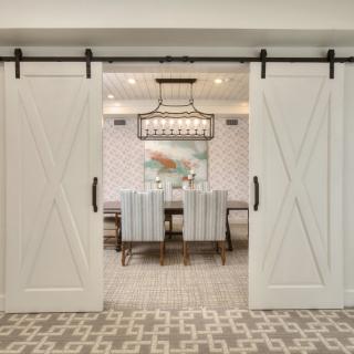 A modern dining room featuring sliding barn doors and a chic chandelier.