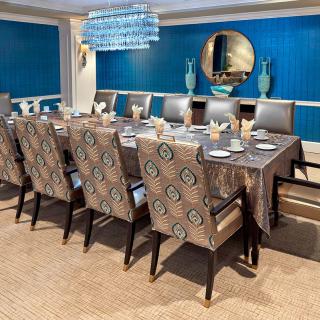 An elegantly decorated dining room with a large table and upholstered chairs, featuring a chandelier and a stylish mirror on a blue wall.