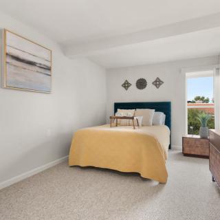 A cozy bedroom with a neatly made bed featuring a yellow blanket, wall decorations, and a window providing natural light.