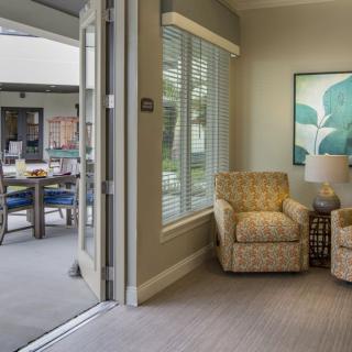 A cozy living room with an armchair and a lamp near a window, opening to a patio.