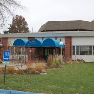 A building entrance with a blue awning and surrounding autumn landscaping.