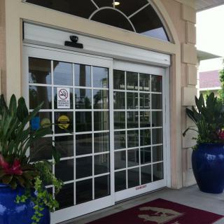 A building entrance featuring a sliding glass door flanked by large decorative blue pots with vibrant plants.