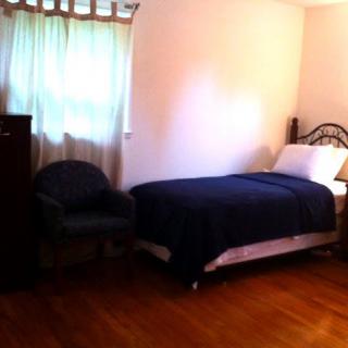 A cozy bedroom with a single bed, chair, and dresser on a wooden floor.