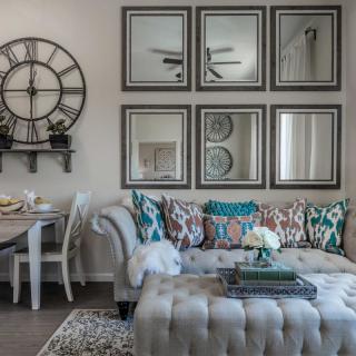 A stylishly decorated living room featuring a tufted sofa with colorful cushions, a set of six framed mirrors, and a large wall clock.