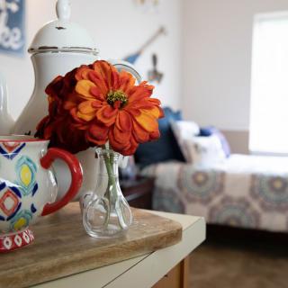A cozy bedroom corner with a vase of vibrant flowers, colorful teapot, and cup.