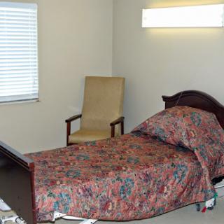 A simple and tidy bedroom featuring a bed with patterned bedding, a chair, and a window.