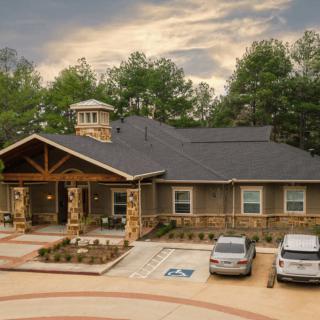 A picturesque house with a parking lot, surrounded by trees under a cloudy sky.