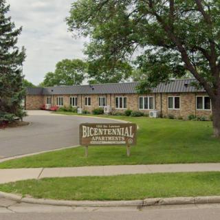 A residential apartment complex with a central driveway and surrounding greenery.