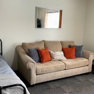 A cozy living area featuring a beige sofa adorned with colorful cushions and a mirror on the wall.