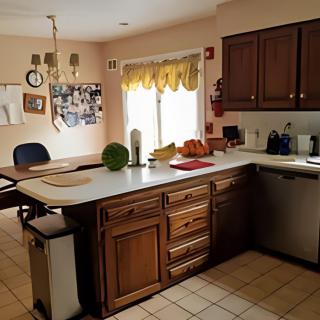 A cozy kitchen with wooden cabinets and a countertop featuring fruits and appliances, adjacent to a dining area.