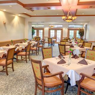 An elegant dining room with neatly arranged tables and chairs, featuring a decorative chandelier.