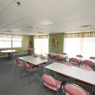 A conference room with several pink chairs around white tables, illuminated by natural light from large windows.