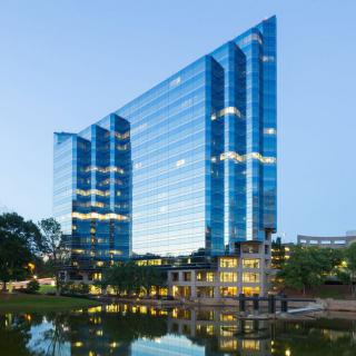 A modern glass facade office building reflecting in the water during twilight.