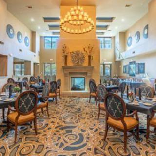 An elegant restaurant dining area with a central chandelier, carpeted floor, and a fireplace.