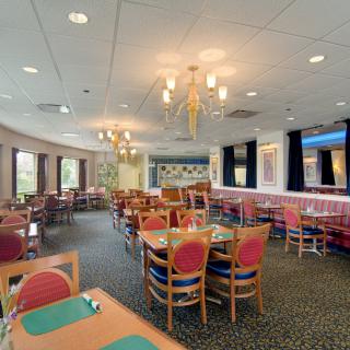 An empty restaurant dining room with neatly arranged tables and chairs, illuminated by chandeliers.