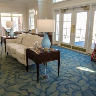 A well-lit living room with a sofa, side table, and lamp on a patterned carpet.