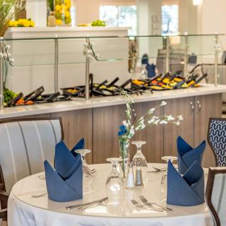 An elegantly set dining table with blue napkins, situated in a restaurant near a buffet.