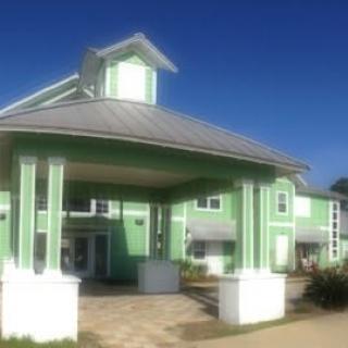 A green building with a prominent entrance featuring columns under a clear blue sky.
