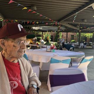 An elderly person sitting outdoors in a decorated area, possibly at a party or gathering.