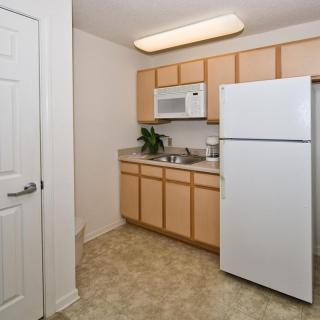 A compact apartment kitchen with wooden cabinets, a refrigerator, and a microwave.