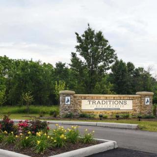Entrance to Traditions community surrounded by trees and flowers.